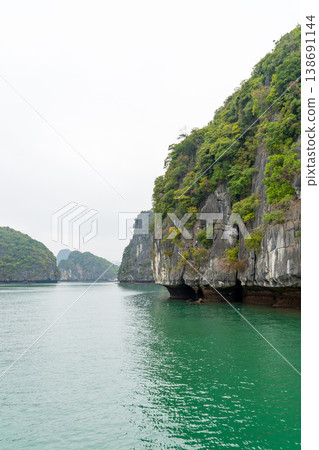 Emerald waters flow between dramatic limestone karsts covered in lush green vegetation in Vietnam's iconic Halong Bay 138691144