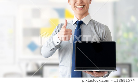 A businessman holding a laptop and making a thumbs-up gesture. A businessman holding a laptop and making a thumbs-up gesture. 138691574