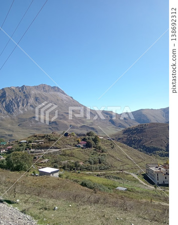 Aerial top view of a North Ossetian village in the Caucasus Mountains, Russia. Dense rooftops and narrow streets nestled between steep mountain slopes Aerial top view of a North Ossetian village in the Caucasus Mountains, Russia. Dense rooftops and narrow streets nestled between steep mountain slopes 138692312