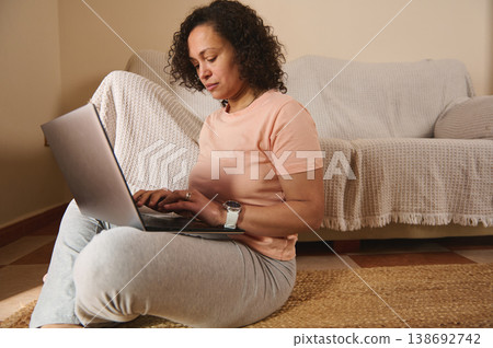 Focused woman working on laptop at home, remote work lifestyle indoors Focused woman working on laptop at home, remote work lifestyle indoors 138692742
