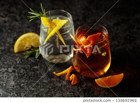 A gin and tonic and an Old Fashioned in frosted glasses on a black table. 138692968