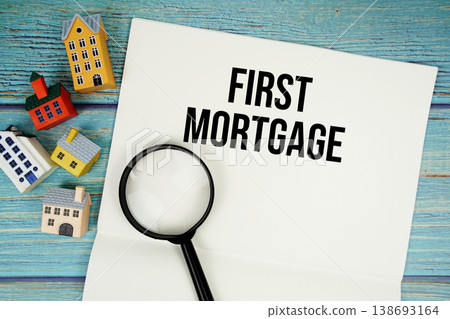 Notepad with "First Mortgage" with magnifying glass and house model on wooden background 138693164