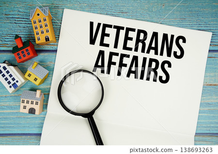 Notepad with "VA Veterans Affairs" with magnifying glass and house model on wooden background Notepad with "VA Veterans Affairs" with magnifying glass and house model on wooden background 138693263