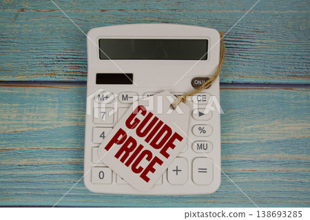 Price tag with "GUIDE PRICE" on calculator on a rustic blue wooden surface 138693285
