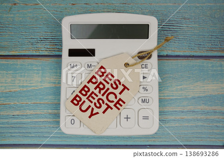 Price tag with "BEST PRICE BEST BUY " on calculator and magnifying glass on a rustic blue wooden surface 138693286