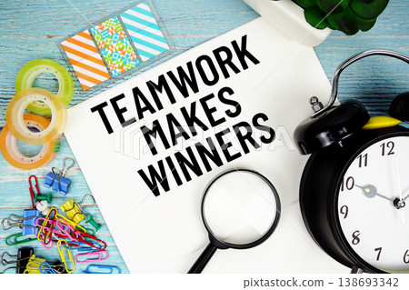 Teamwork Makes Winners text on a paper surrounded by office supplies, a magnifying glass, and a clock on a blue wooden surface Teamwork Makes Winners text on a paper surrounded by office supplies, a magnifying glass, and a clock on a blue wooden surface 138693342