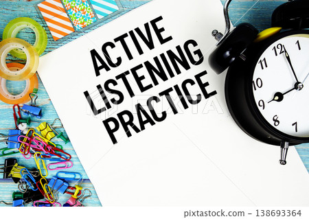 Active Listening Practice text on a paper surrounded by office supplies and a clock on a blue wooden surface 138693364