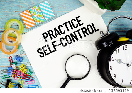 Practice Self-Control text on a paper surrounded by office supplies, a magnifying glass, and a clock on a blue wooden surface 138693369