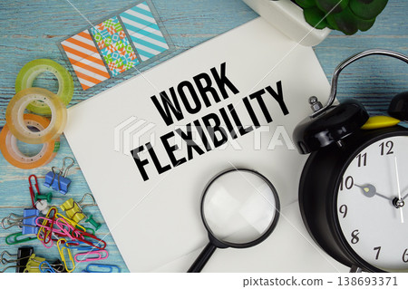 Work Flexibility text on a paper surrounded by office supplies, a magnifying glass, and a clock on a blue wooden surface Work Flexibility text on a paper surrounded by office supplies, a magnifying glass, and a clock on a blue wooden surface 138693371