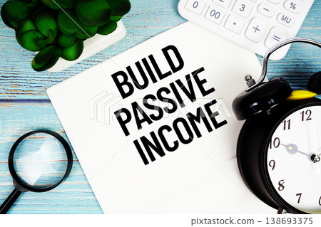 Build Passive Income message written on paper placed on a blue wooden surface, alongside a magnifying glass, a clock, a calculator, and a small plant Build Passive Income message written on paper placed on a blue wooden surface, alongside a magnifying glass, a clock, a calculator, and a small plant 138693375