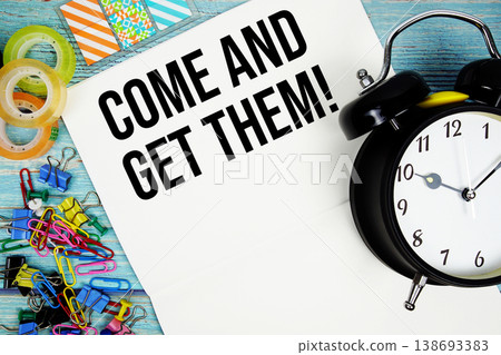Come And Get Them! text with alarm clock and colorful office supplies on a blue wooden surface Come And Get Them! text with alarm clock and colorful office supplies on a blue wooden surface 138693383