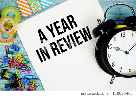 A Year In Review text with alarm clock and colorful office supplies on a blue wooden surface 138693403