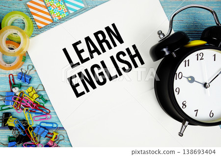 Learn English text with alarm clock and colorful office supplies on a blue wooden surface 138693404