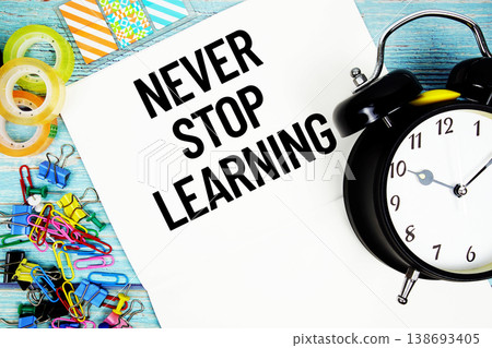 Never Stop Learning text on a paper surrounded by office supplies and a clock on a blue wooden surface Never Stop Learning text on a paper surrounded by office supplies and a clock on a blue wooden surface 138693405