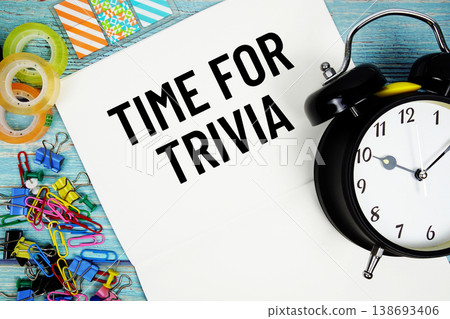 Time For Trivia text on a paper surrounded by office supplies and a clock on a blue wooden surface Time For Trivia text on a paper surrounded by office supplies and a clock on a blue wooden surface 138693406