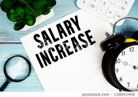 Salary Increase written on paper placed on a blue wooden surface, alongside a magnifying glass, a clock, a calculator, and a small plant Salary Increase written on paper placed on a blue wooden surface, alongside a magnifying glass, a clock, a calculator, and a small plant 138693409