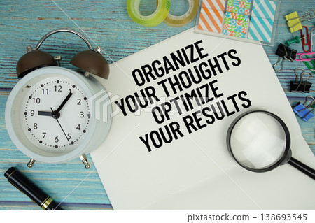 Organize Your Thoughts. Optimize Your Results text on a paper surrounded by office supplies, a magnifying glass, and a clock on a blue wooden surface Organize Your Thoughts. Optimize Your Results text on a paper surrounded by office supplies, a magnifying glass, and a clock on a blue wooden surface 138693545