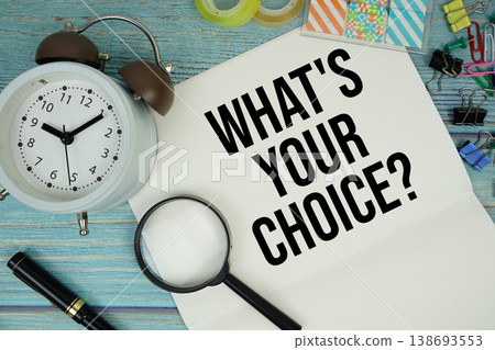 What's Your Choice? text on a paper surrounded by office supplies, a magnifying glass, and a clock on a blue wooden surface 138693553