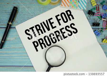 Strive For Progress text written on notepad with magnifying glass flat lay on wooden background Strive For Progress text written on notepad with magnifying glass flat lay on wooden background 138693557