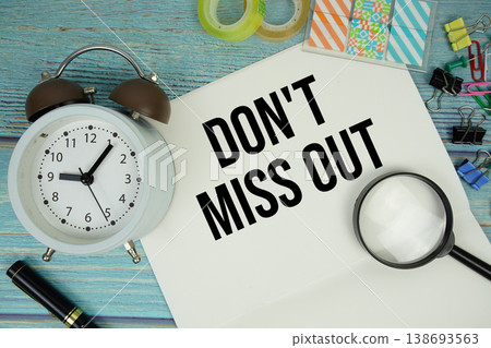 Don't Miss Out text written on notepad with alarm clock and magnifying glass flat lay on wooden background 138693563