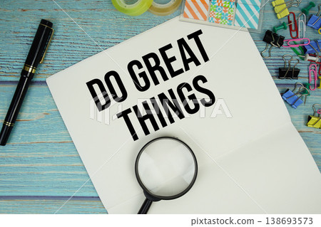 Do Great Things text on a paper surrounded by office supplies and magnifying glass on a blue wooden surface 138693573