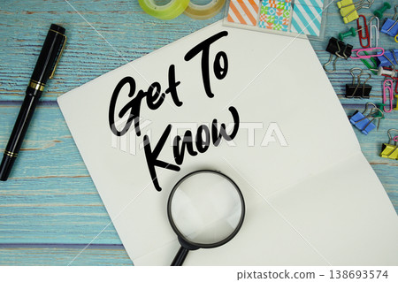Get To Know text on a paper surrounded by office supplies and magnifying glass on a blue wooden surface 138693574