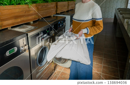 Woman loading laundry into washing machine at modern self service laundromat interior lifestyle scene Woman loading laundry into washing machine at modern self service laundromat interior lifestyle scene 138694036