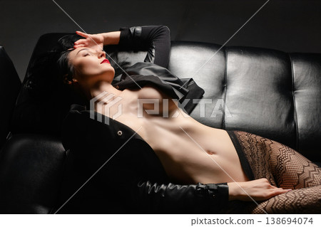 Elegant woman with red lipstick in an open jacket relaxing on a black leather sofa. Elegant woman with red lipstick in an open jacket relaxing on a black leather sofa. 138694074