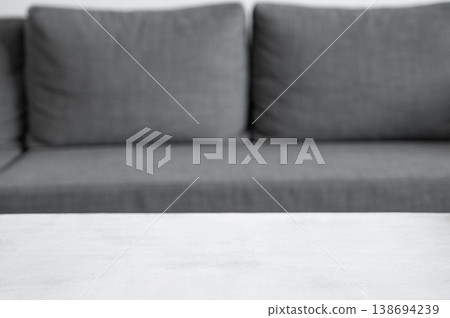 An empty, light textured tabletop against a blurred sofa in a light interior backdrop. 138694239