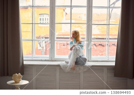 Easygoing lighthaired woman sitting by window contemplating urban view Easygoing lighthaired woman sitting by window contemplating urban view 138694493