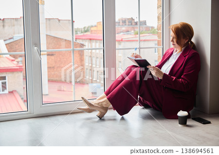 Consultant in burgundy attire prepares for evening reflections by window Consultant in burgundy attire prepares for evening reflections by window 138694561
