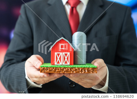 A businessman holds a farm with a plot of land in his hands. Agribusiness and farming. Investment in agriculture supports food production, land ownership and rural economic development. 138694620