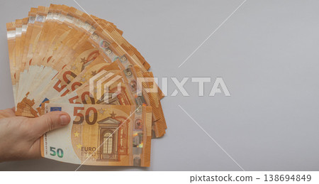 Female hands holding a large fan of 50 Euro banknotes against a white background. High-volume cash concept with orange bills and extensive copy space for design 138694849