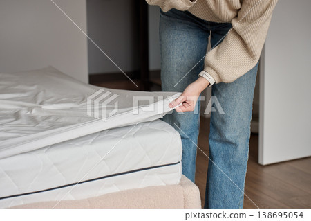 Woman pulling white fitted sheet off mattress in bedroom Woman pulling white fitted sheet off mattress in bedroom 138695054