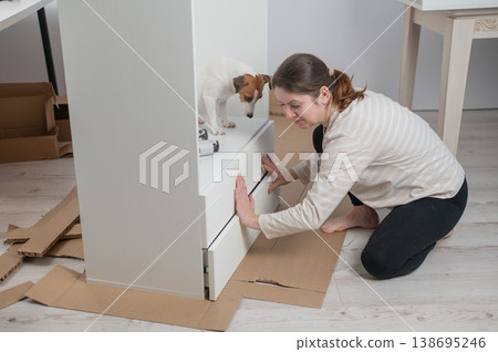 A Caucasian woman assembles furniture with her cute dog. A Caucasian woman assembles furniture with her cute dog. 138695246