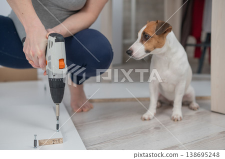 A Caucasian woman uses a screwdriver to tighten a screw while assembling a cabinet. 138695248