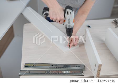 A Caucasian woman uses a screwdriver to tighten a screw while assembling a cabinet. 138695250