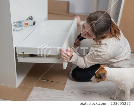 A Caucasian woman assembles furniture with her cute dog. A Caucasian woman assembles furniture with her cute dog. 138695255