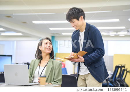A female systems engineer gives instructions on development requirements to a junior engineer who is taking notes. A female systems engineer gives instructions on development requirements to a junior engineer who is taking notes. 138696341