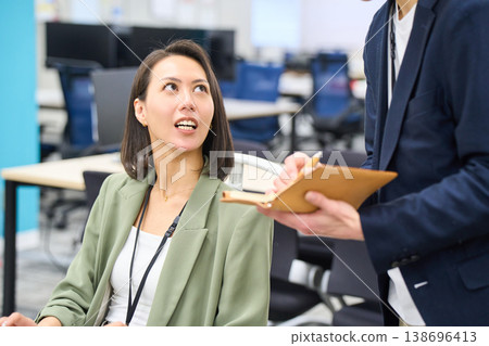 A female systems engineer gives instructions on development requirements to a junior engineer who is taking notes. A female systems engineer gives instructions on development requirements to a junior engineer who is taking notes. 138696413