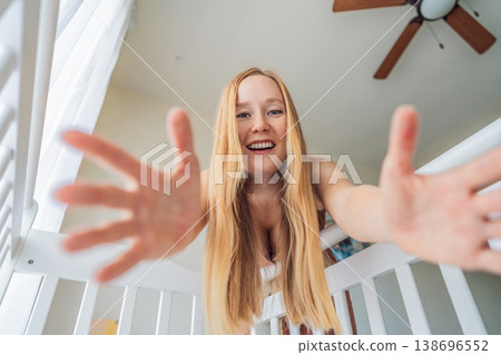 Mother looking into baby crib and playing with newborn at home. Loving mom bonding with infant, smiling and interacting. Parenting care, early childhood development and emotional connection concept 138696552