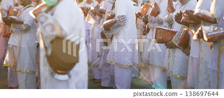 Participants in white clothing line up holding folded orange robes as soft sunlight reveals intricate lace details and hands within a medium to large ceremonial setting. Participants in white clothing line up holding folded orange robes as soft sunlight reveals intricate lace details and hands within a medium to large ceremonial setting. 138697644