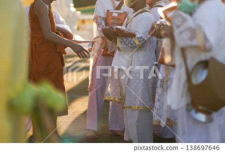 Participants in white clothing line up holding folded orange robes as soft sunlight reveals intricate lace details and hands within a medium to large ceremonial setting. Participants in white clothing line up holding folded orange robes as soft sunlight reveals intricate lace details and hands within a medium to large ceremonial setting. 138697646