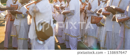 Participants in white clothing line up holding folded orange robes as soft sunlight reveals intricate lace details and hands within a medium to large ceremonial setting. Participants in white clothing line up holding folded orange robes as soft sunlight reveals intricate lace details and hands within a medium to large ceremonial setting. 138697647