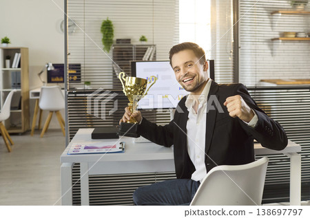 Smiling manager holds golden trophy celebrating victory at bright modern office Smiling manager holds golden trophy celebrating victory at bright modern office 138697797