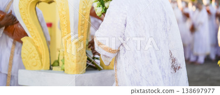 A temple marker stands above arranged lotus incense and candles as fresh lotus bundles and folded robes rest nearby with a blurred statue adding depth to the warm sacred ceremonial setting. 138697977