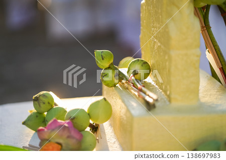 A temple marker stands above arranged lotus incense and candles as fresh lotus bundles and folded robes rest nearby with a blurred statue adding depth to the warm sacred ceremonial setting. 138697983
