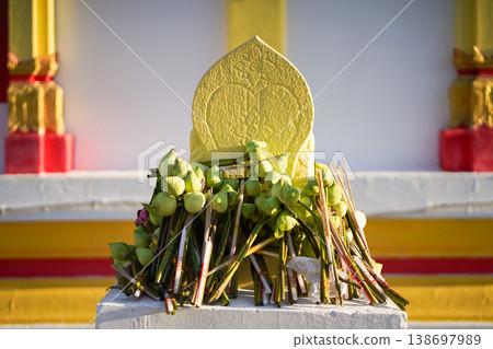 A temple marker stands above arranged lotus incense and candles as fresh lotus bundles and folded robes rest nearby with a blurred statue adding depth to the warm sacred ceremonial setting. A temple marker stands above arranged lotus incense and candles as fresh lotus bundles and folded robes rest nearby with a blurred statue adding depth to the warm sacred ceremonial setting. 138697989
