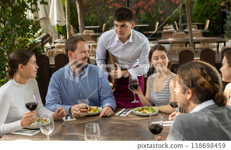 Group of positive friends placing an order to a young waiter on the terrace of an open air restaurant 138698459