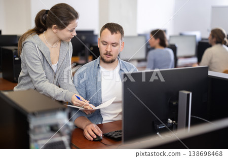 Man and woman discussing document while working on computer 138698468